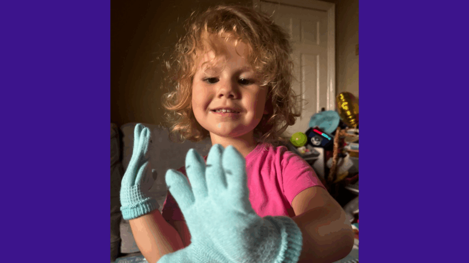 Olive is smiling and looking down at the gloves she had to wear due to the complications from sepsis on her fingers