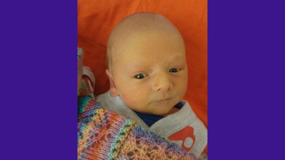 Gemma, Olive and Thomas are all crouched on the floor and smiling. Olive is wearing a colourful rain coat.