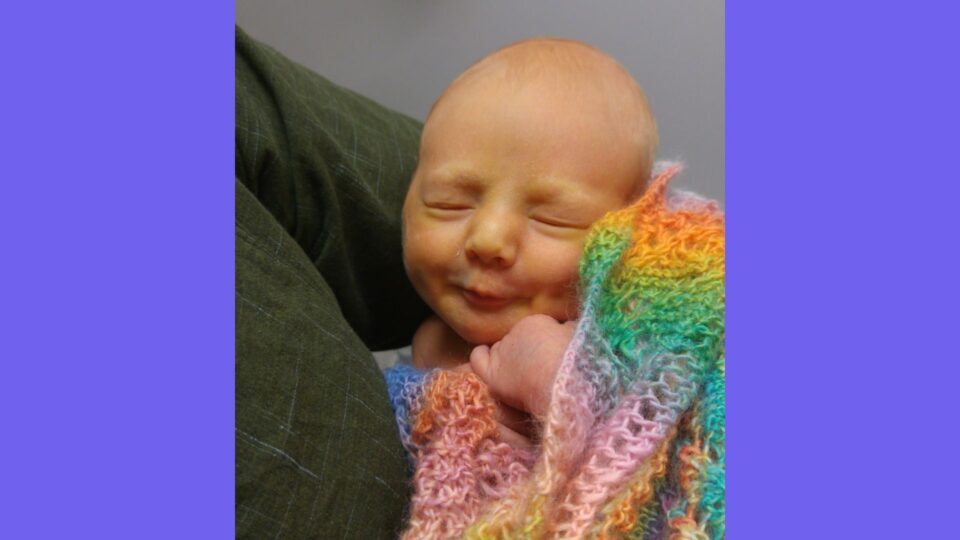 Kit is sleeping in someone's arms is doing an adorable, scrunched up smile.