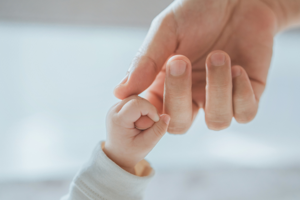 A baby's hand grasping their parent's index finger