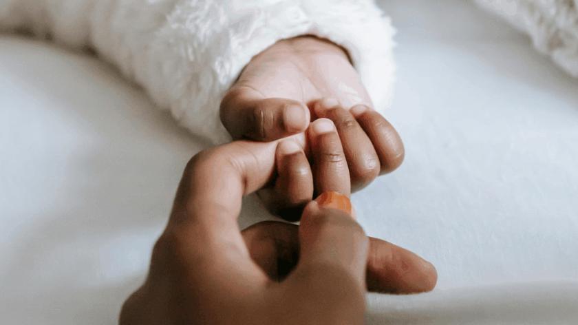 A baby's hand grasping their parent's index finger