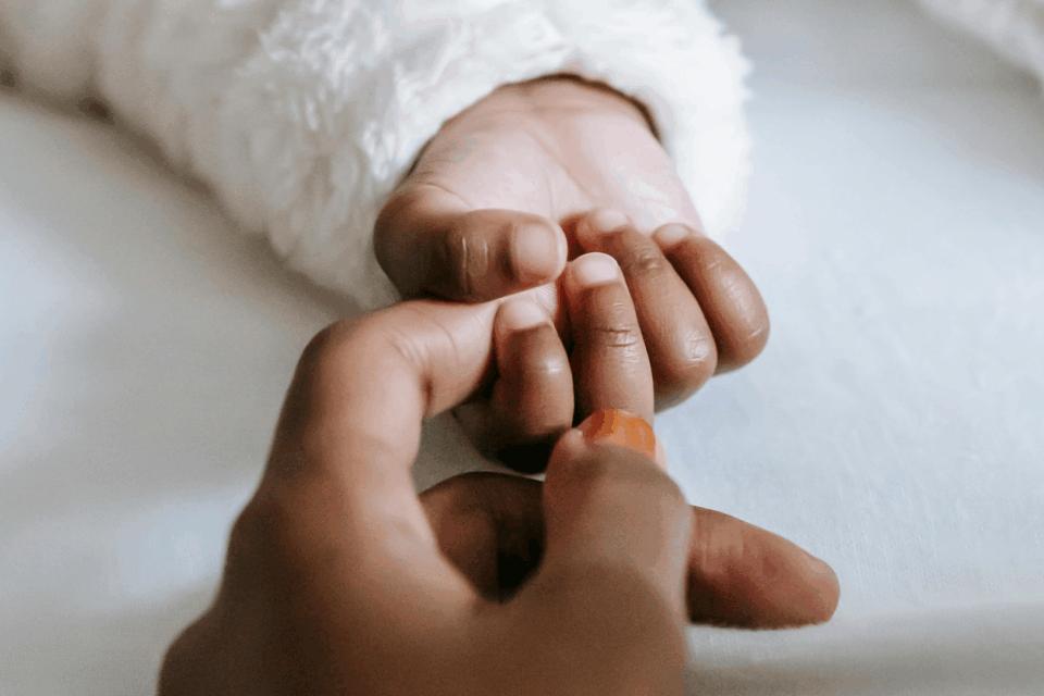 A baby's hand grasping their parent's index finger