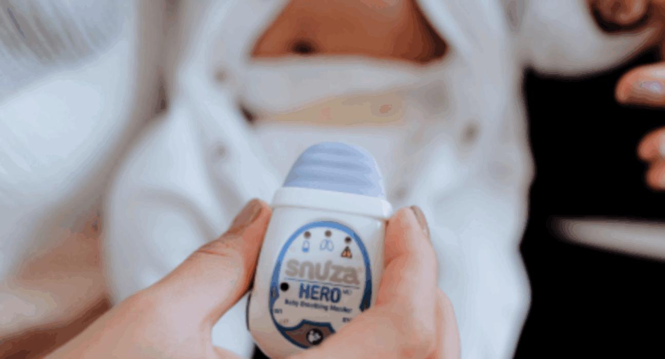 Snuza HeroMD monitor being held up with a baby in a babygrow in the background.