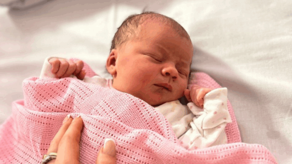 Baby Violet asleep on her back with a pink blanket on her.