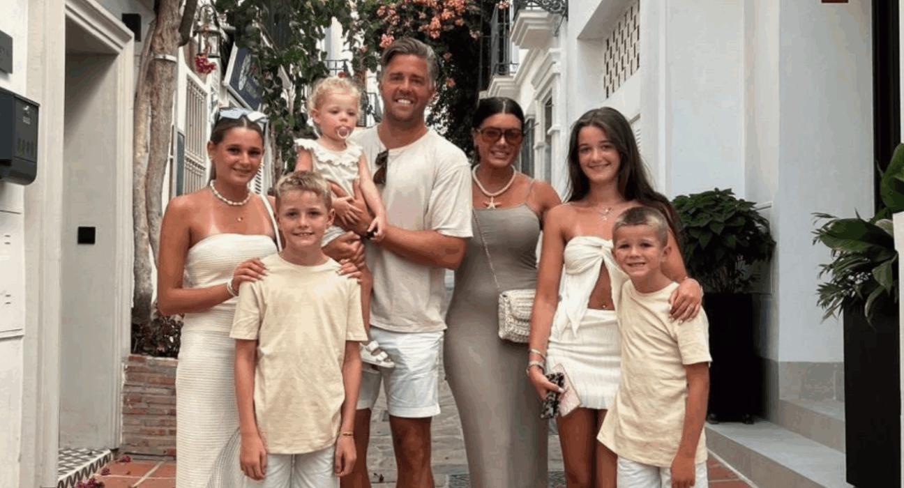 Matt holding his little girl, with his partner beside him and four other children. All wearing white on holiday.