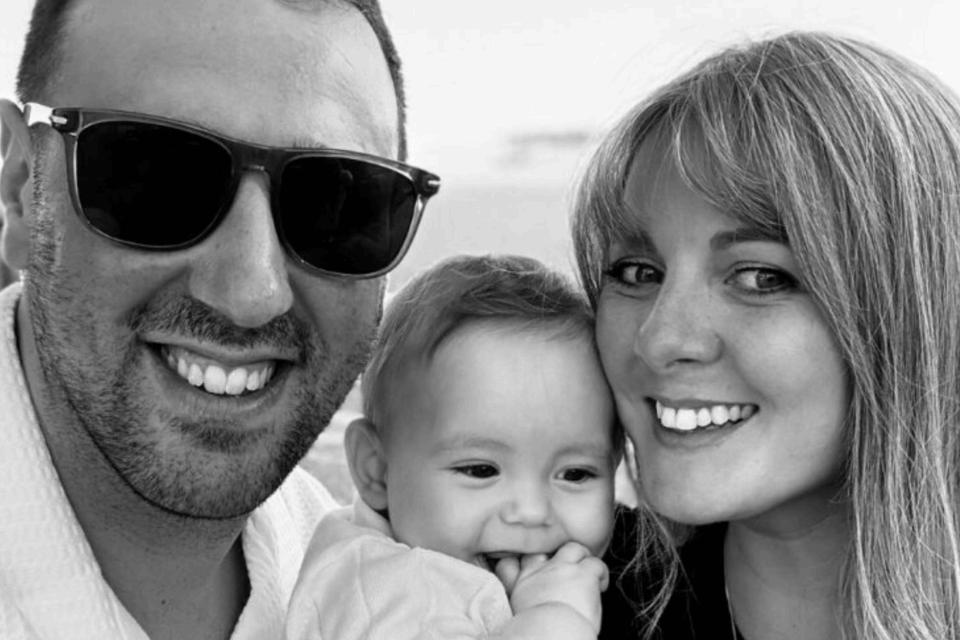 Leah and Josh smiling at the camera, holding baby George.