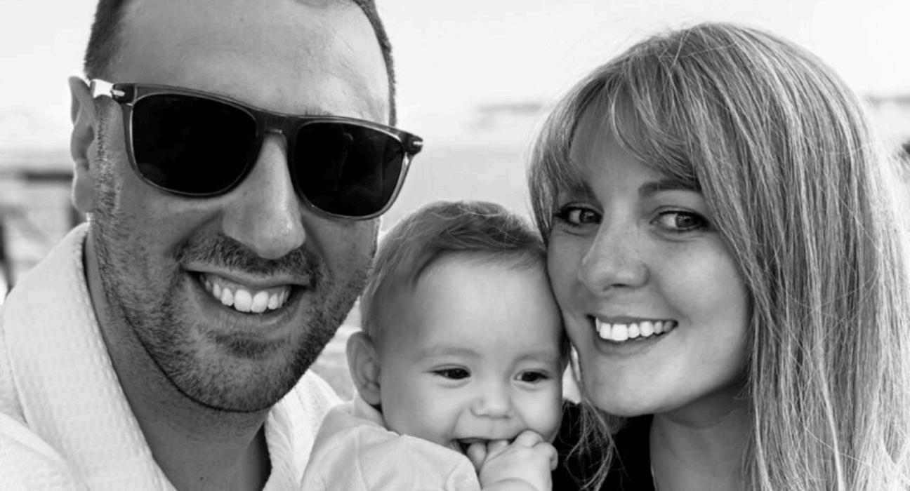 Leah and Josh smiling at the camera, holding baby George.