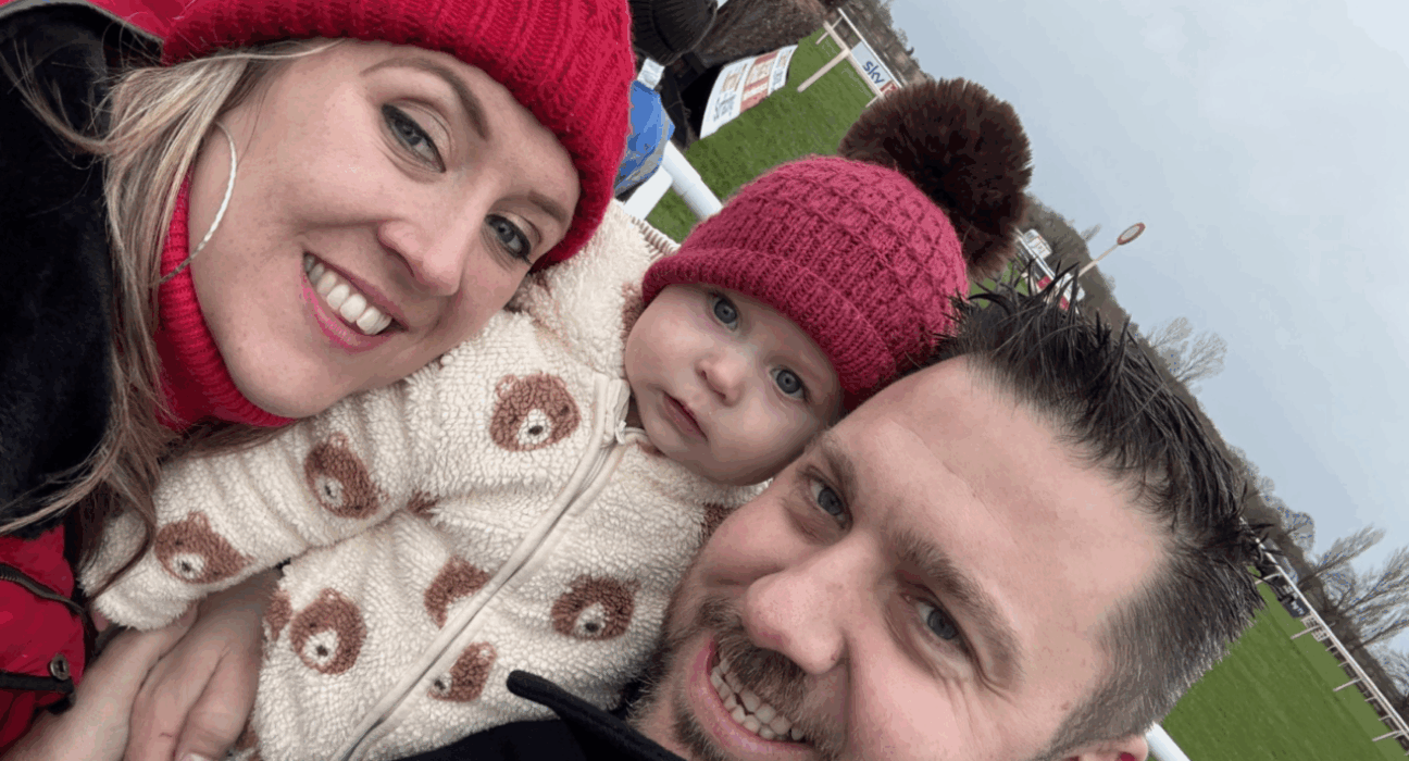 Helen wearing a red wooly hat, Faith also wearing a red hat, and Stephen, all smiling at the camera outdoors.