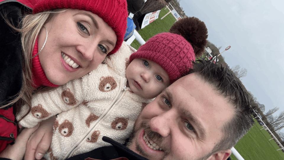 Helen wearing a red wooly hat, Faith also wearing a red hat, and Stephen, all smiling at the camera outdoors.