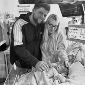 Hayley and Dimitri standing by the bed that Violet is sleeping in.