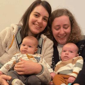 Izzy and Laura sitting next to each other on the sofa, holding Alo and Jovie.