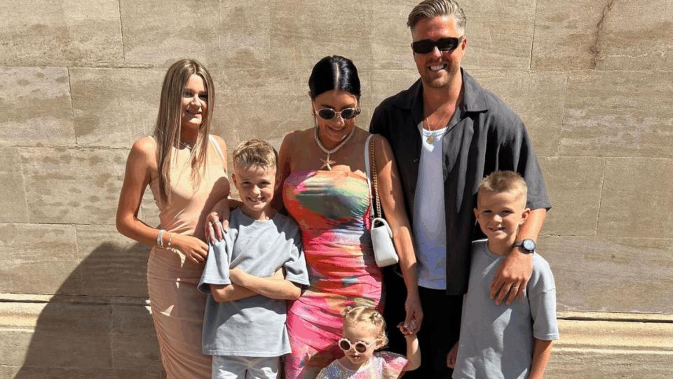 Matt standing outdoors with his family on a sunny day, smiling at the camera.