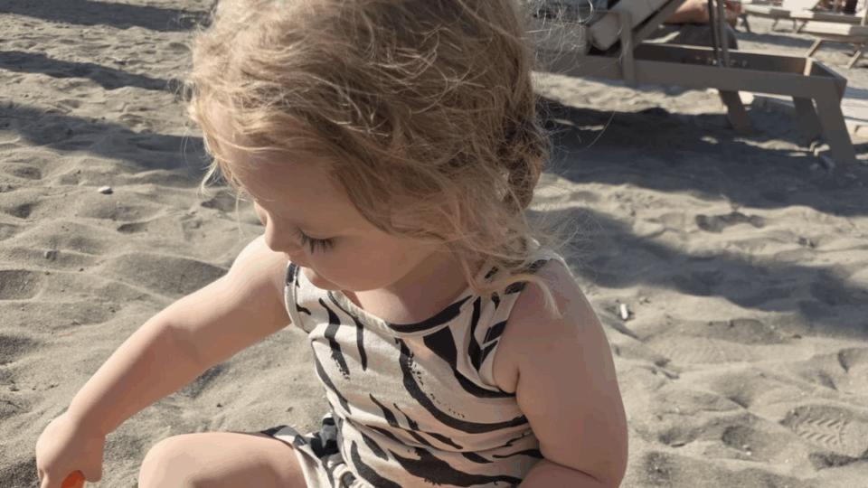 Aerith sitting on the sand at the beach, playing.