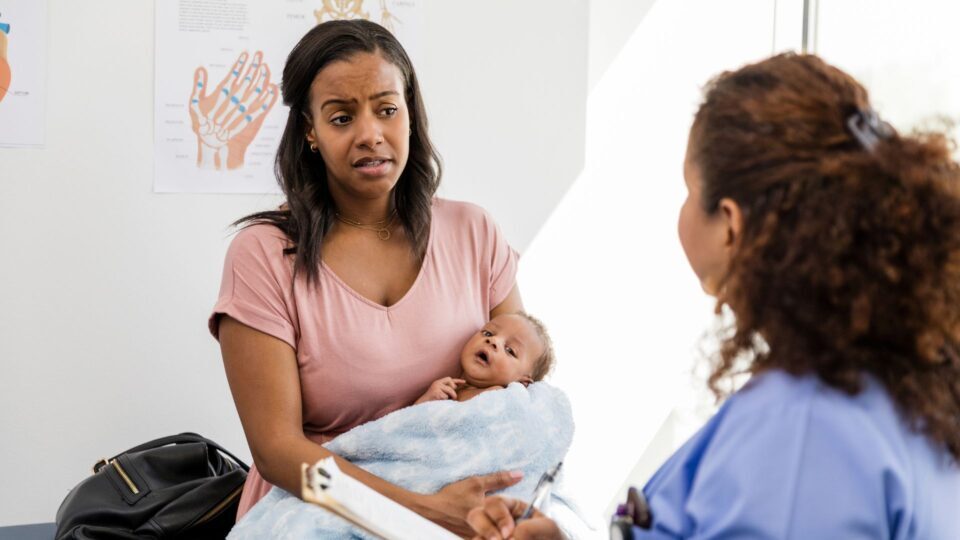 A young mother holds her baby while talking to a doctor. Concern is evident on the mother's face.