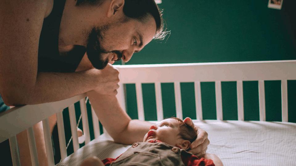Dad putting baby to sleep on their back in a cot.