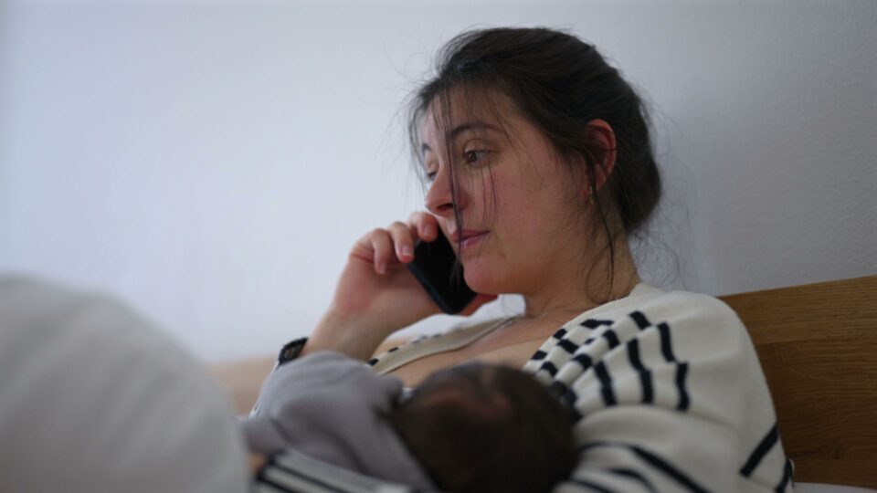Mother multitasking while her baby sleeps peacefully in her arms, speaking on the phone with a thoughtful expression. the quiet balance between caring for a sleeping newborn and handling daily responsibilities
