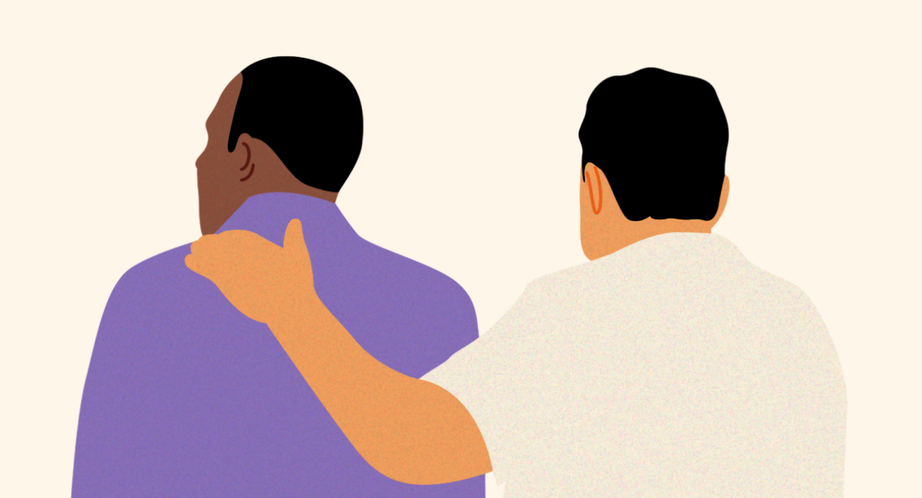 Two men with their back to us. One man has a supportive arm around the other.