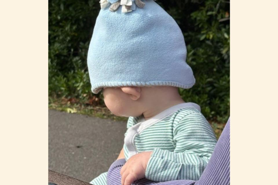 Baby Jonah wearing a blue hat, and a stripy top, facing away from the camera.