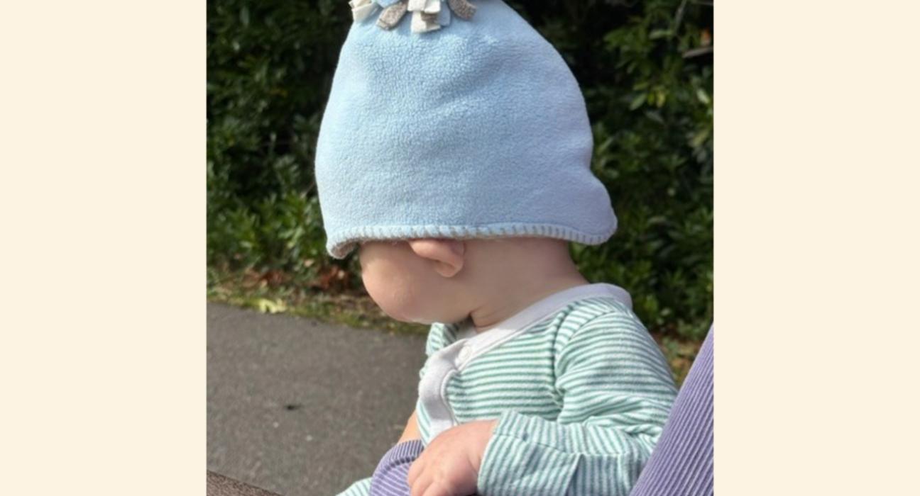 Baby Jonah wearing a blue hat, and a stripy top, facing away from the camera.