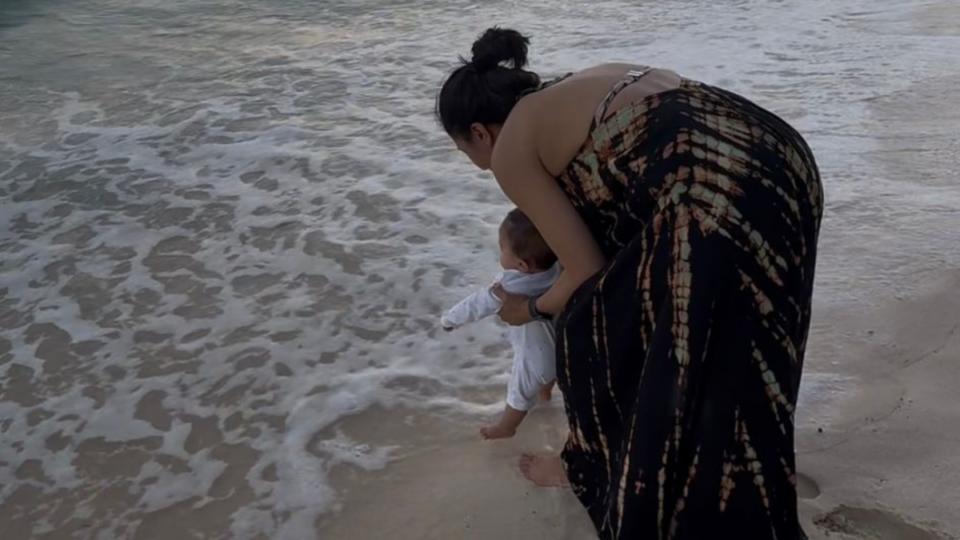 Harpal standing behind Lara on the beach, holding her up on her feet.