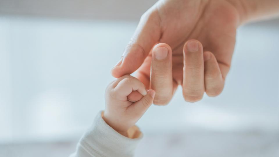 A baby's hand grasping their parent's index finger