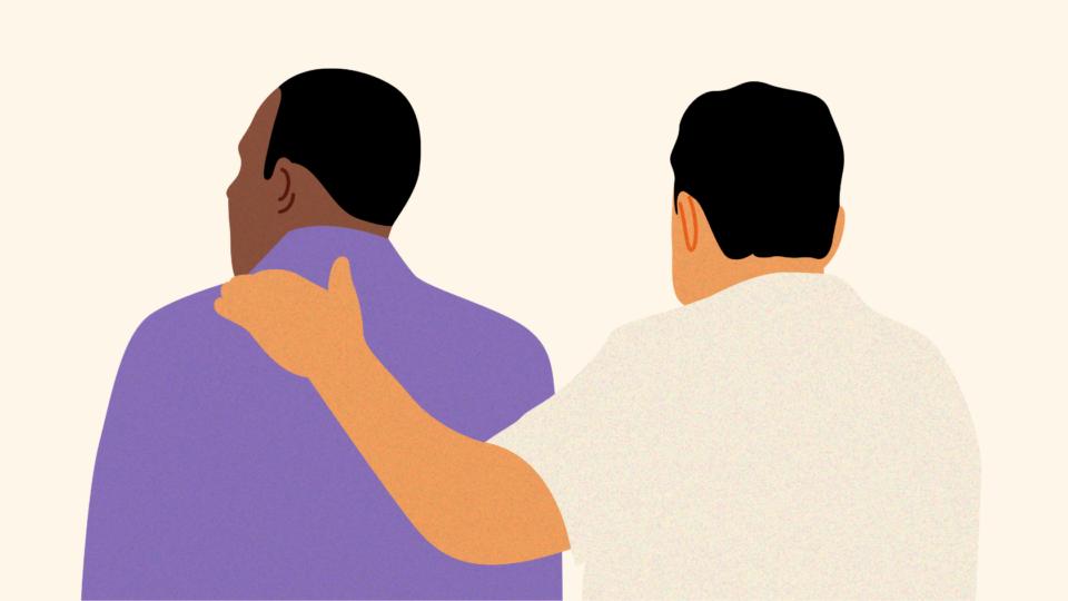 Two men with their back to us. One man has a supportive arm around the other.