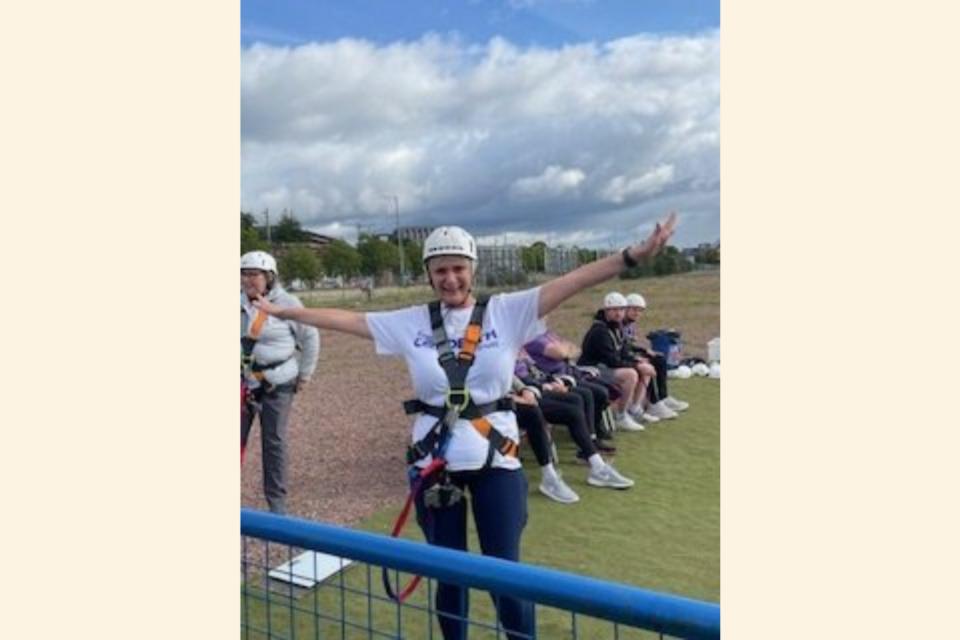 Margaret in a harness and a helmet with arms outstretched, about to do a bungee jump.