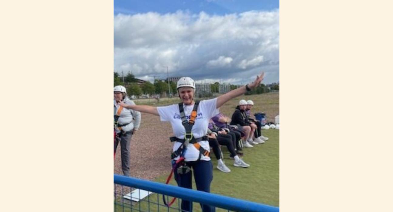 Margaret in a harness and a helmet with arms outstretched, about to do a bungee jump.
