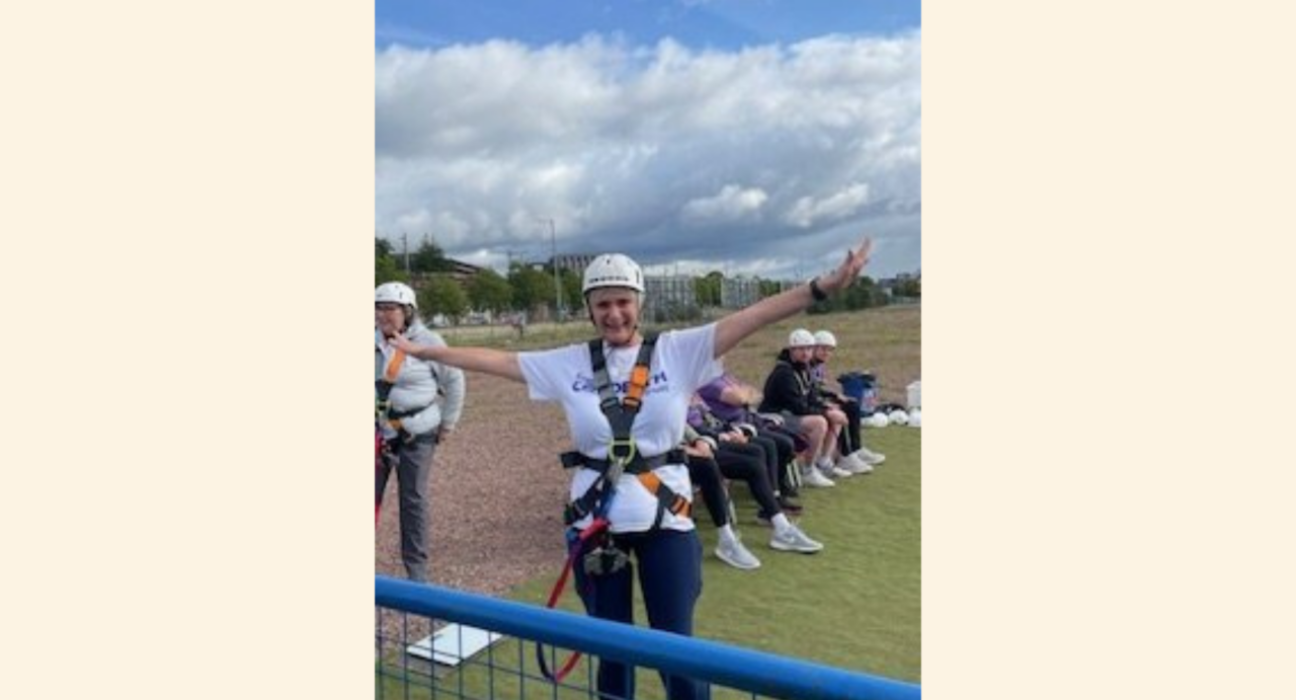 Margaret in a harness and a helmet with arms outstretched, about to do a bungee jump.
