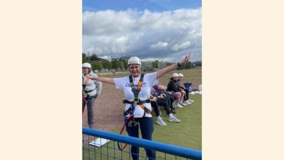 Margaret in a harness and a helmet with arms outstretched, about to do a bungee jump.