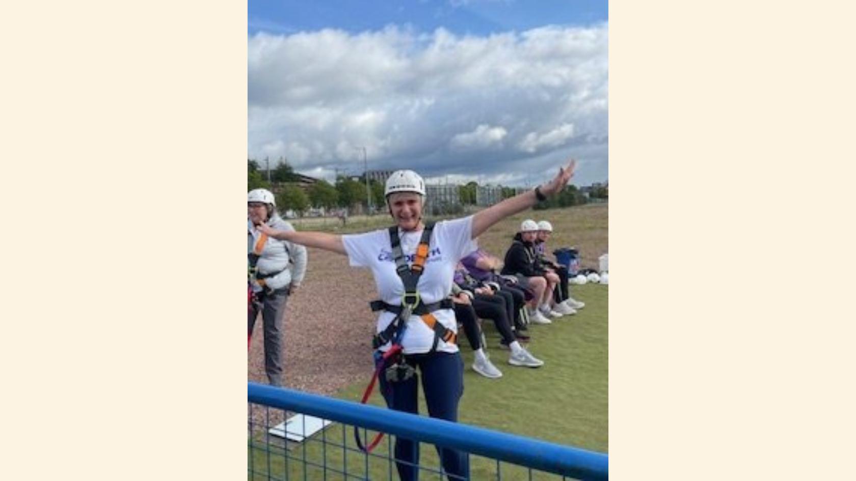 Margaret in a harness and a helmet with arms outstretched, about to do a bungee jump.