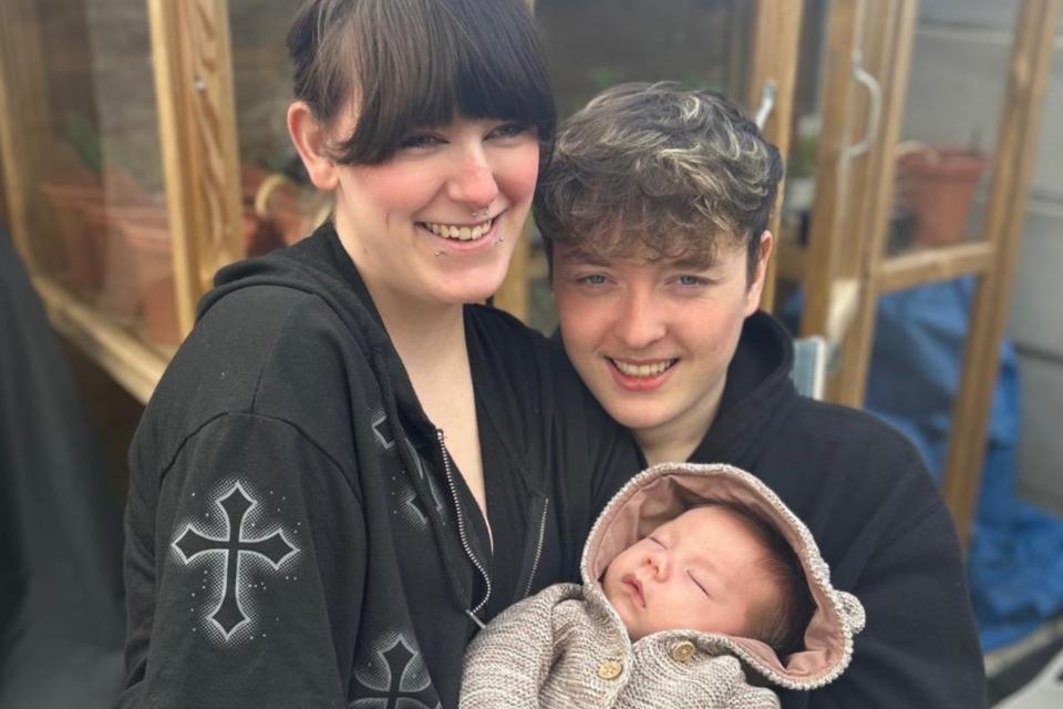 Lilly and James smiling at the camera, holding Theo.