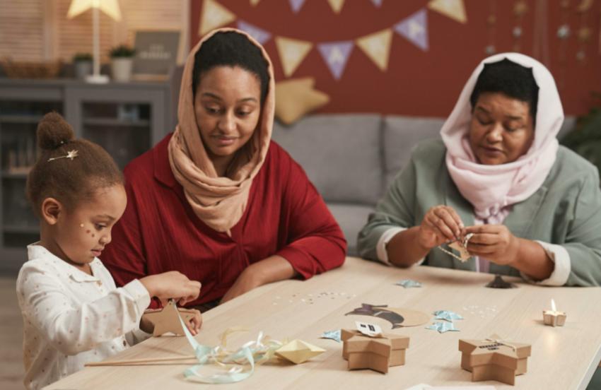 Two women and a child sitting at a table doing arts and crafts together.