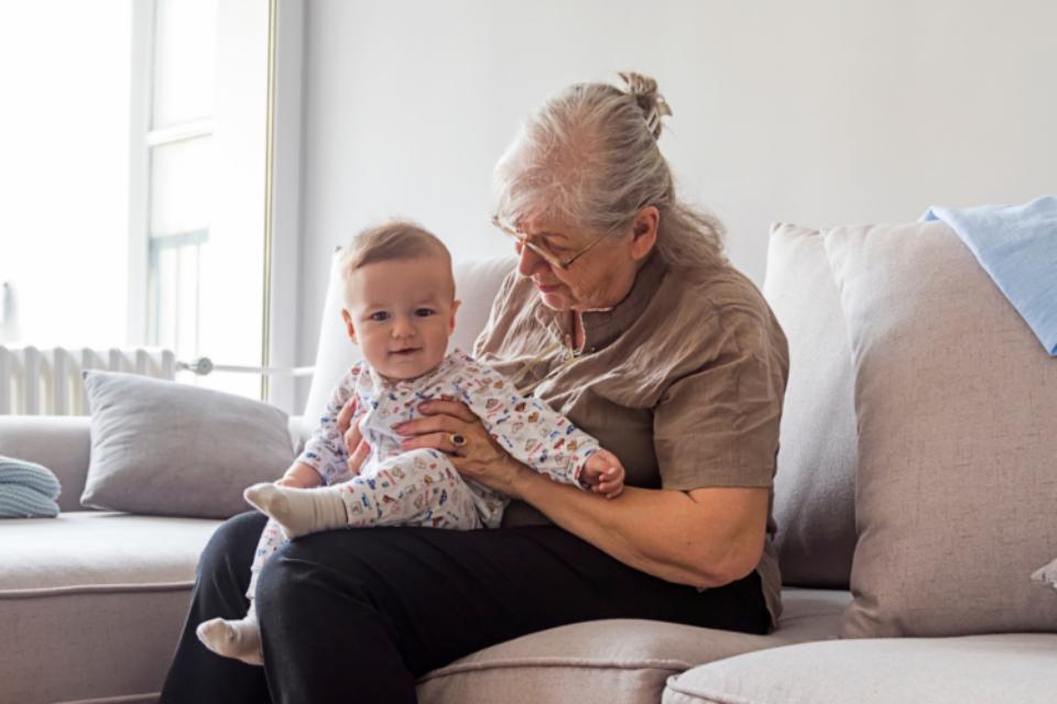 Grandmother sitting on a sofa with a baby on her lap wearing a baby grow.
