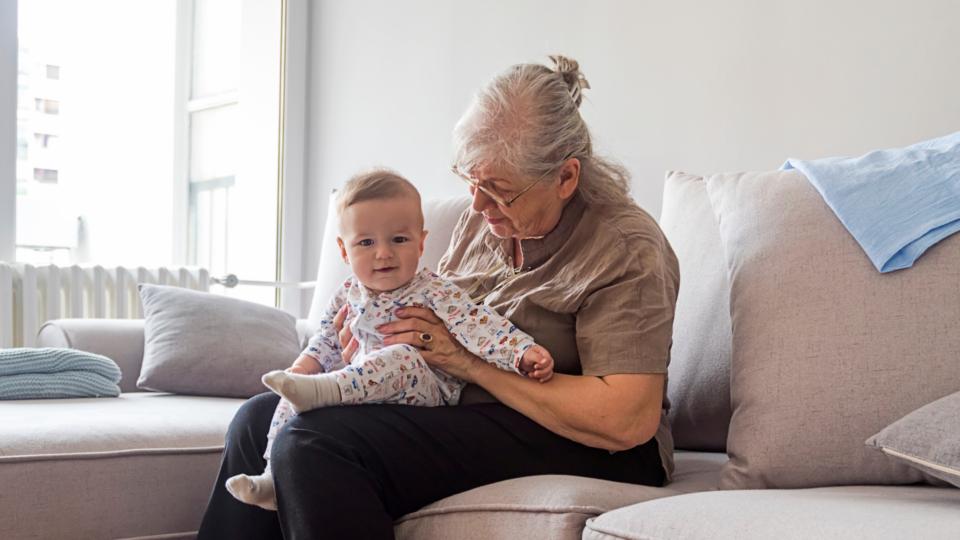 Grandmother sitting on a sofa with a baby on her lap wearing a baby grow.