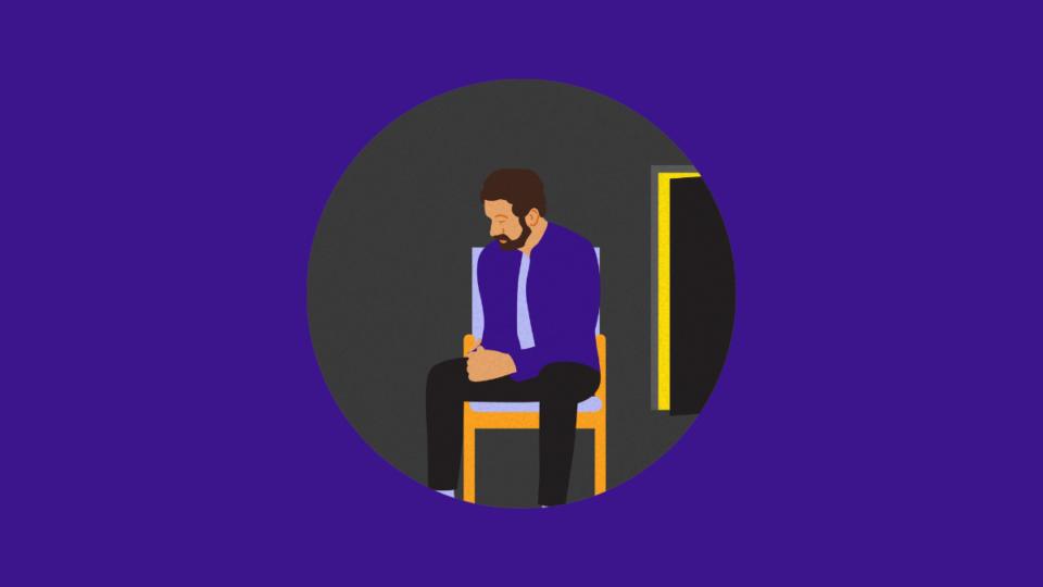 Man sitting on a chair in darkness, his elbows resting on his legs.