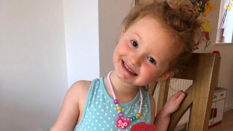 Amy wearing a blue top and a chunky pink necklace, smiling.