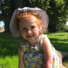 Amy wearing a sun hat and sun dress, smiling at the camera