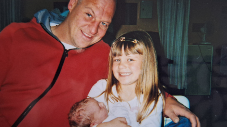Sue's husband wearing a red hoodie, and their daughters smiling at the camera