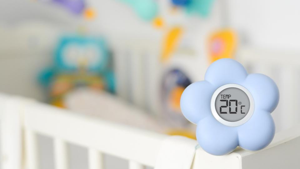 A thermometer, shaped as a flower, sits on a baby's cot.
