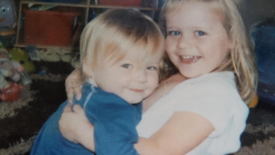 Sue's daughters hugging each other and looking at the camera.