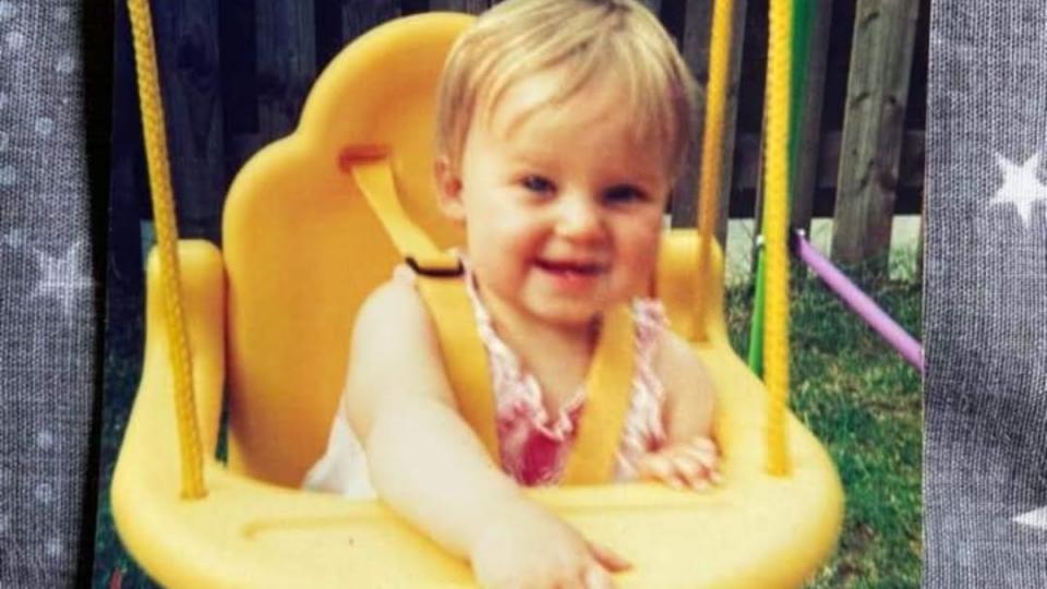 Sue's daughter smiling, sitting in a yellow swing.