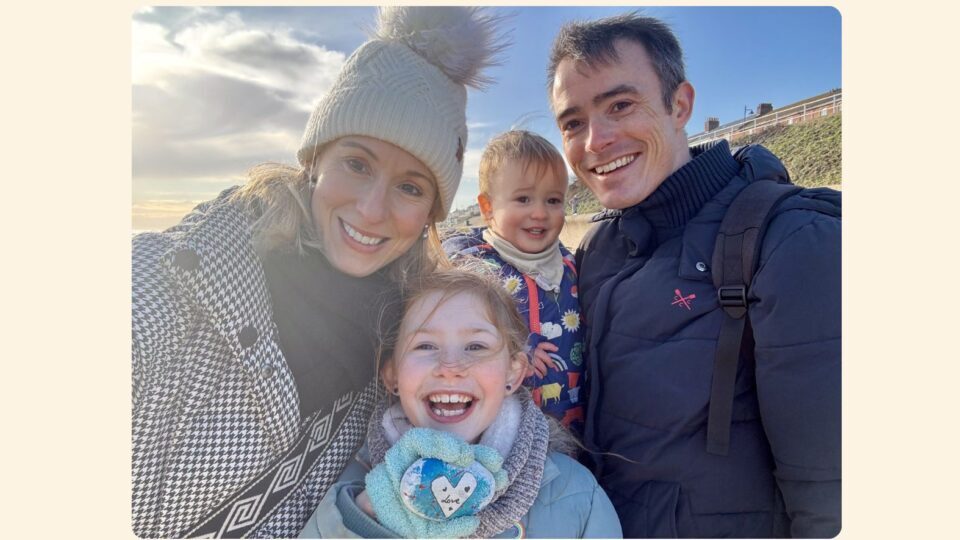 A family photo of Laura, Kieran, Ella and Oliver on the beach. They are wrapped up in hats, coats and scarves and all smiling widely.