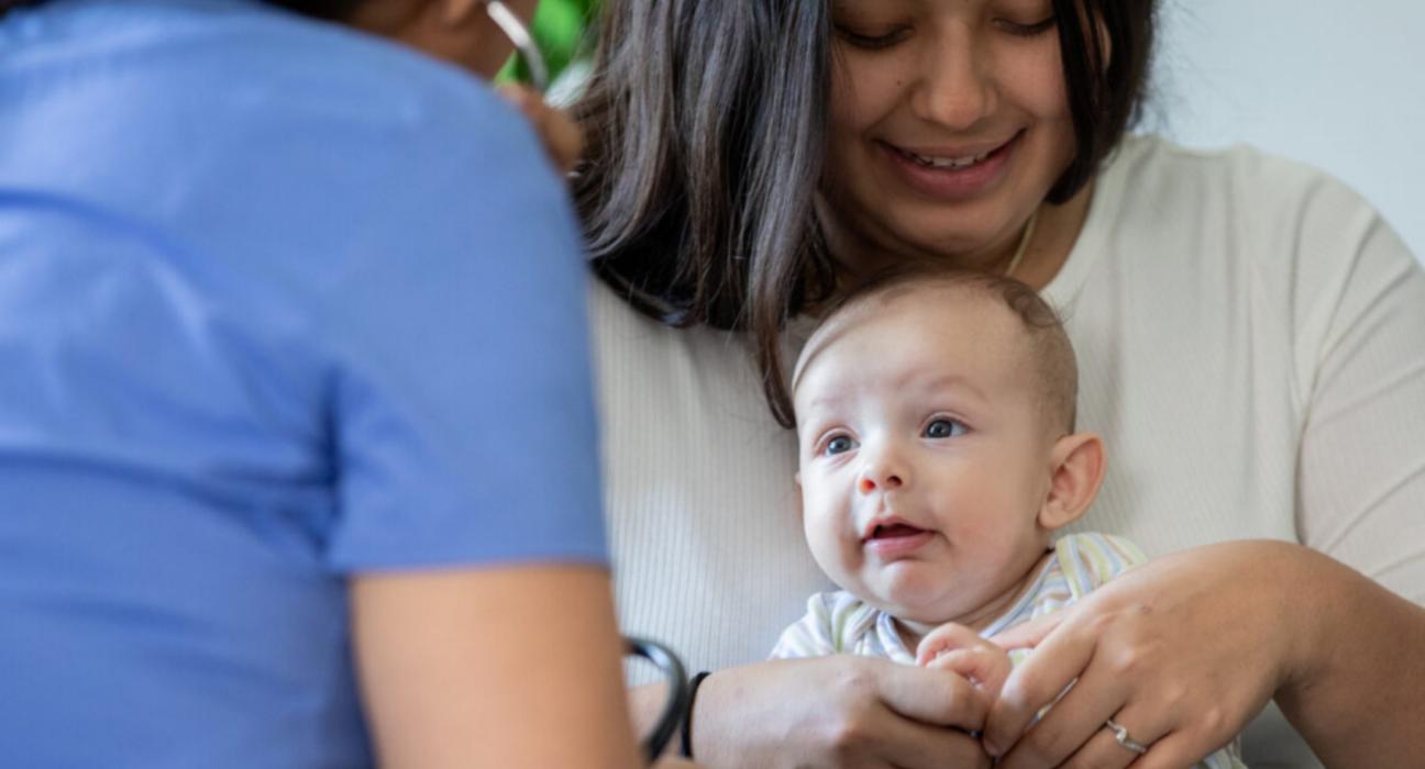 Lady holding her baby. There is also a health professional with their back to us.