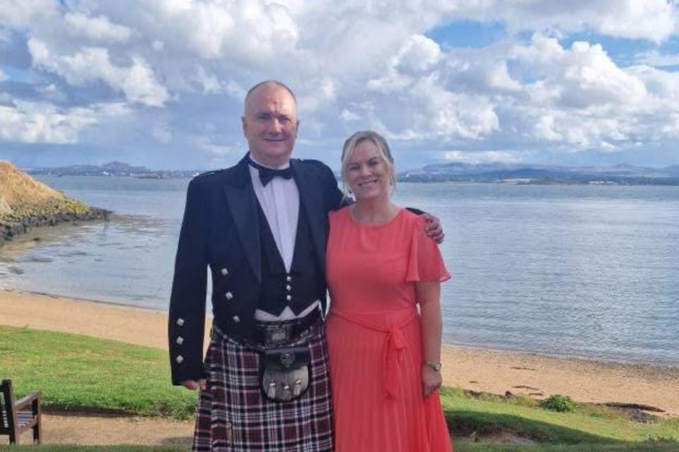 Fiona and David. David is wearing a kilt and Fiona is wearing an orange dress.