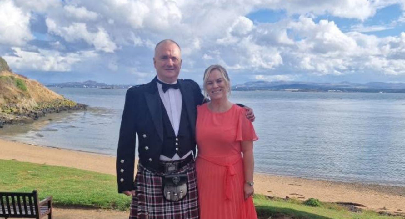 Fiona and David. David is wearing a kilt and Fiona is wearing an orange dress.