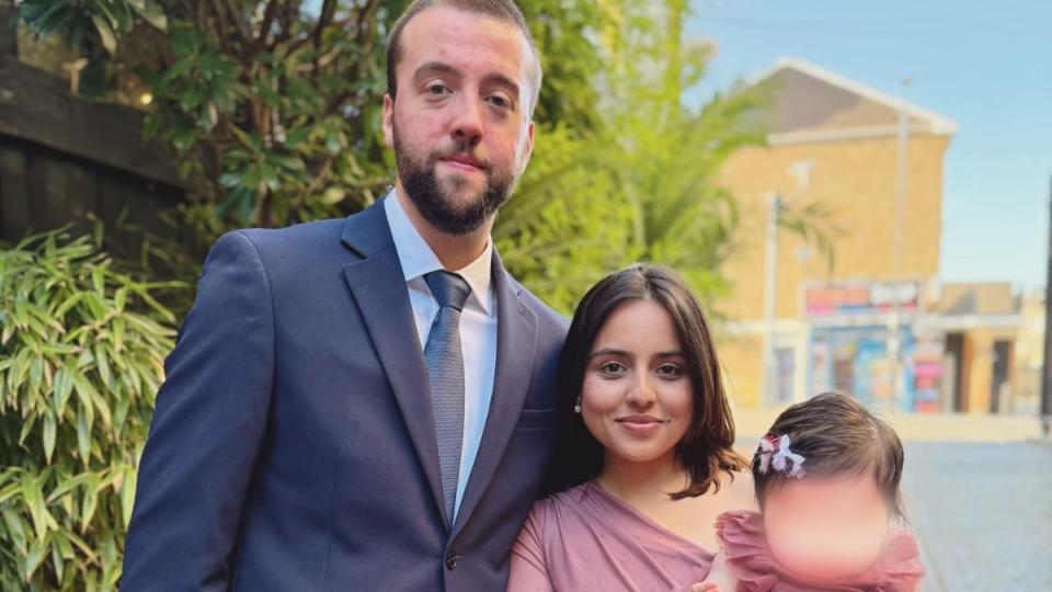 Murihah wearing a pink dress, next to her husband in a suit. She is holding Alannah