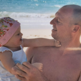 Sue's husband holding Caelyn, on the beach.