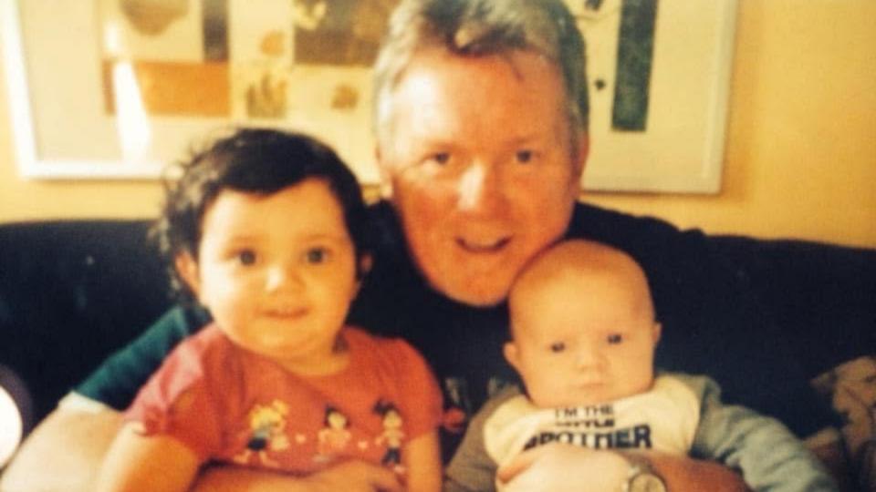 Kirsty's family. A male sitting on a sofa with his arms around two children, all smiling.