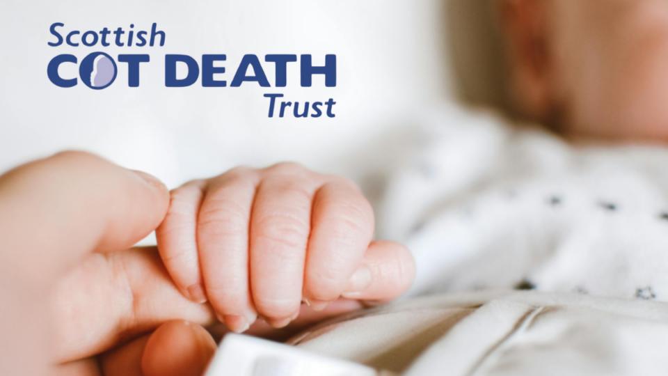 Close up of a baby's hand holding an adult's finger. The Scottish Cot Death Trust logo is in the top left corner.